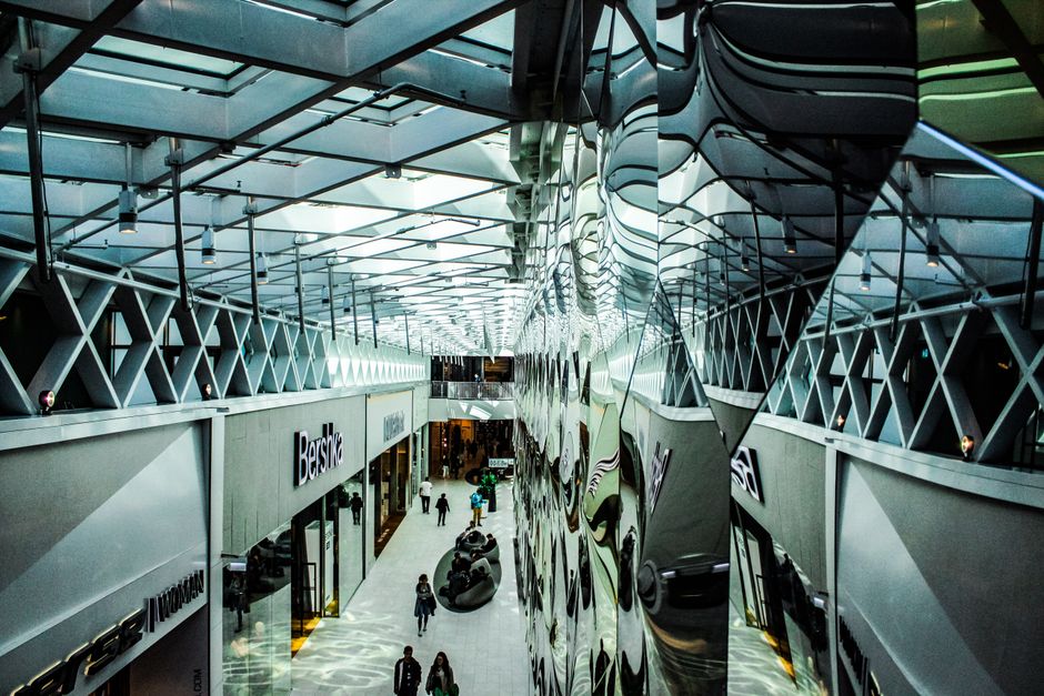 Interior view of Westfield London shops in W12, showcasing a spacious shopping mall with a high ceiling and extensive glass windows allowing natural light to illuminate the area. The floor is made of